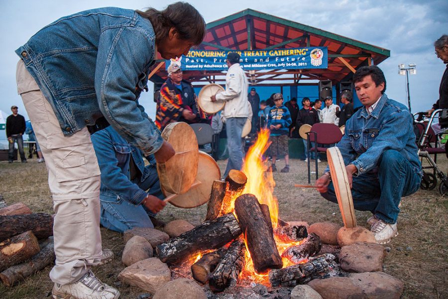 Three First Nation drummers around a fire