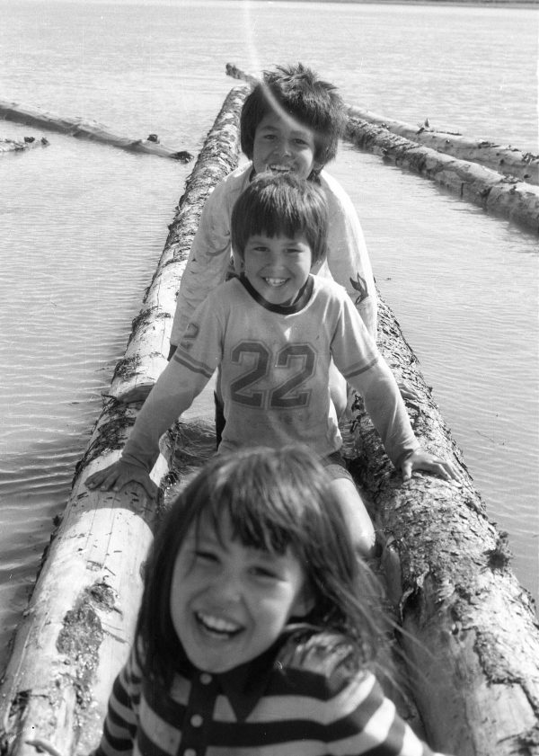 Black and white - three kids playing with driftwood on water