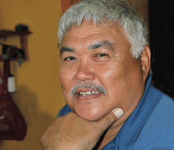 coloured image of a man with grey hair and moustache wearing a blue shirt and smiling