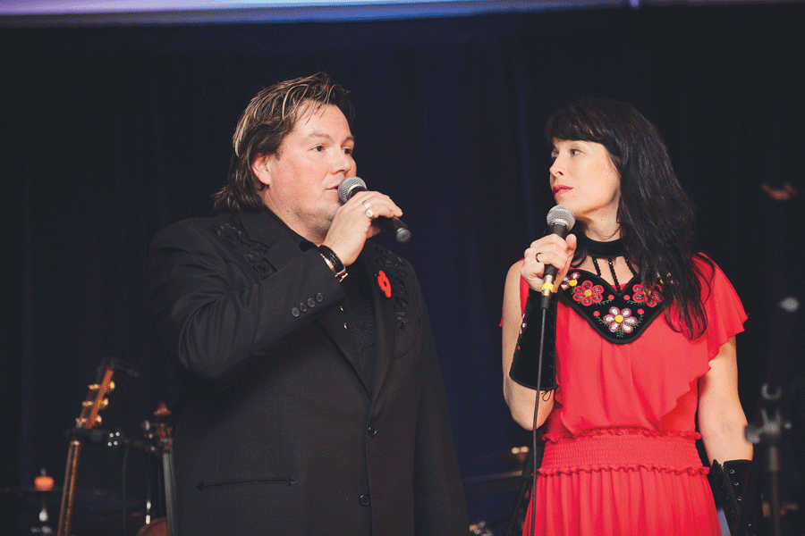 coloured image of a man dressed in black and a woman dressed in red signing with each other
