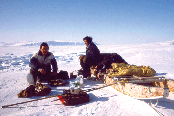 Two men sit on sleds on the snow and drink tea