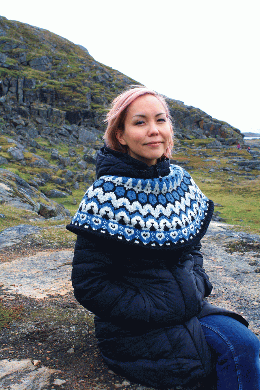 Woman sitting on a rock smiling off into the distance with nature around her