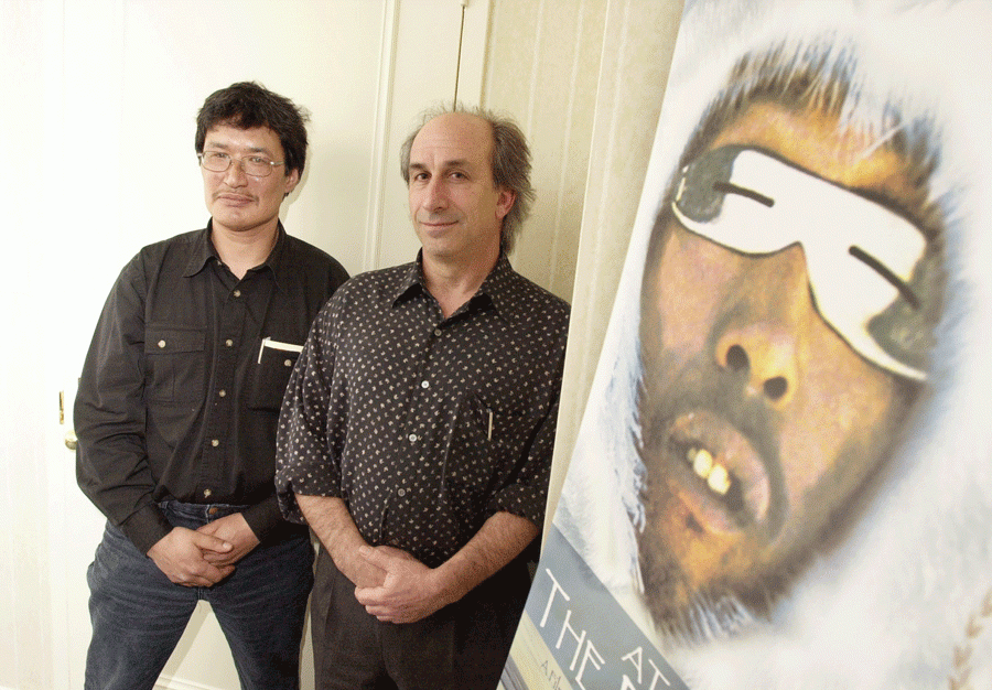 Two men lean against a wall with a poster of a person on it