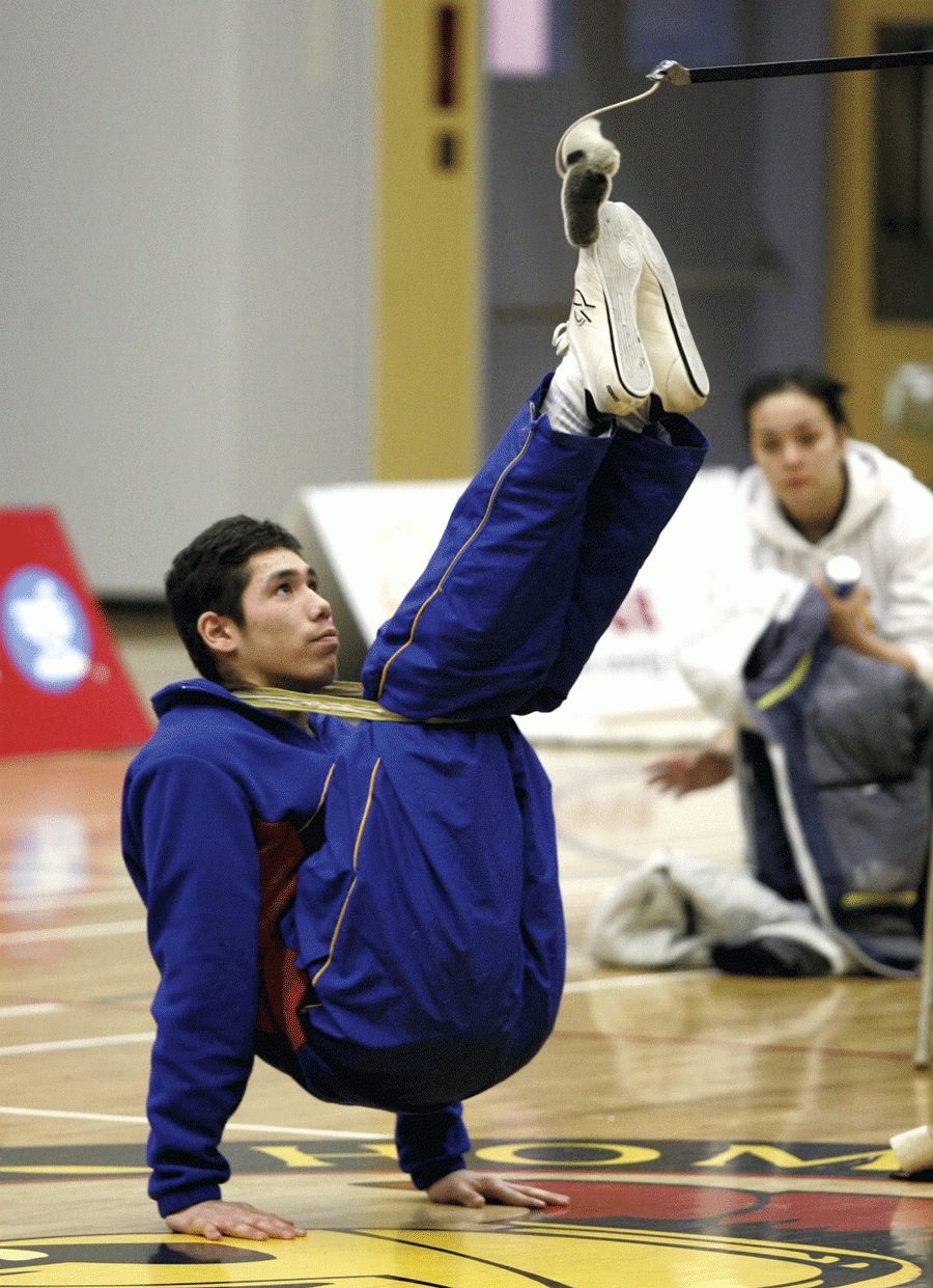 Boy using his hands to hold his legs up in front to kick a ball on a stick