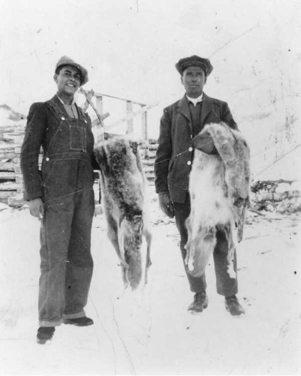 Two men stand holding skins