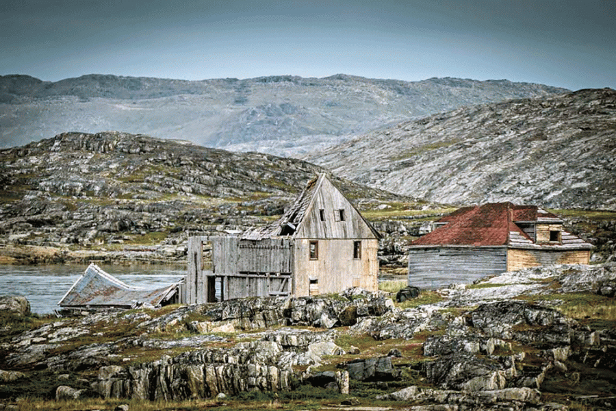 An old shack surrounded by rock, hills and grass