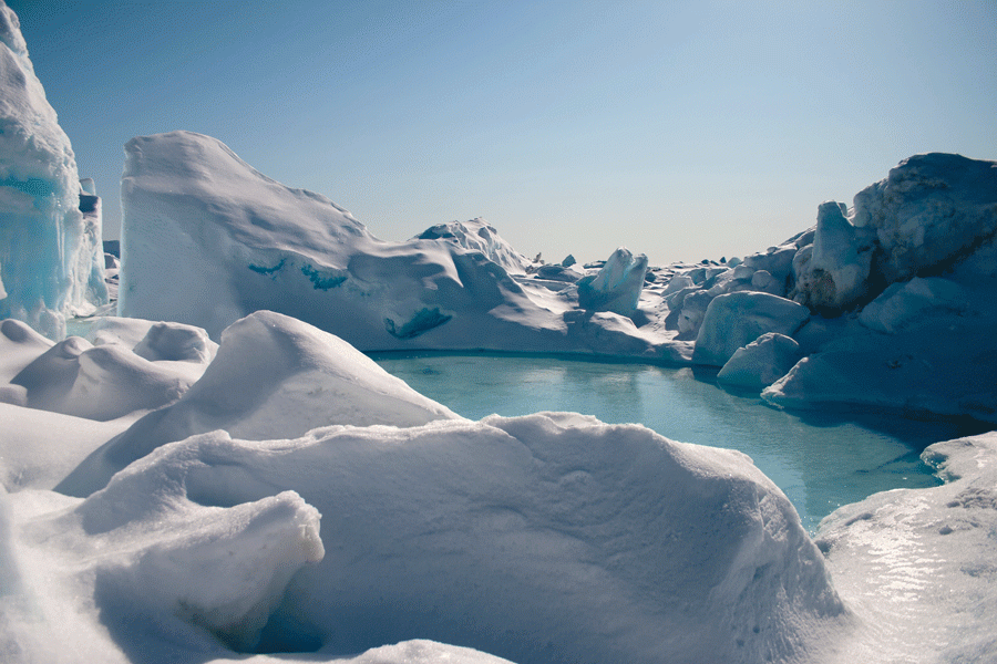 Snow forms small peaks surrounding a turquoise pond