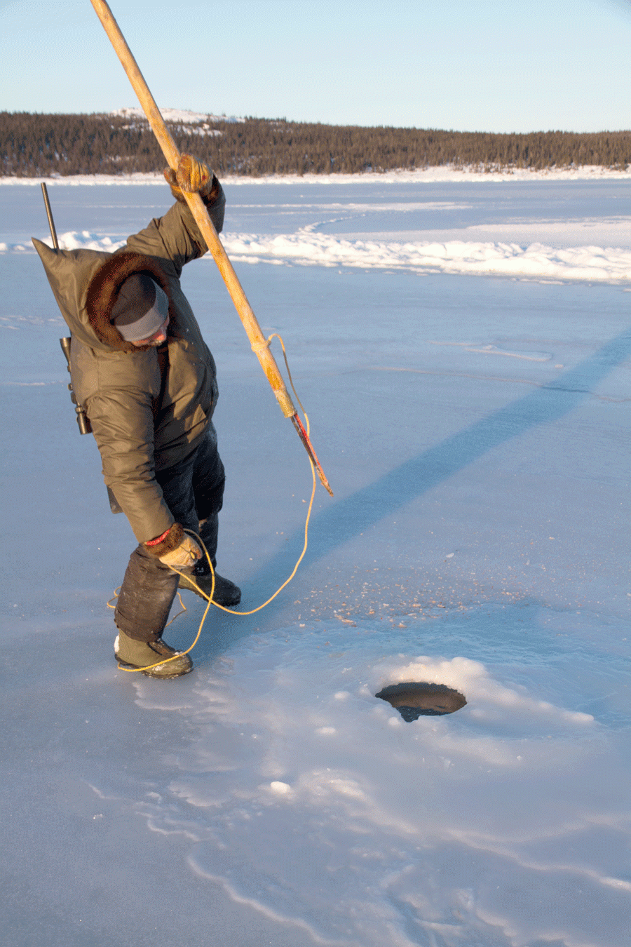 A man holds a spear over a hole in the ice ready to spear a fish or seal